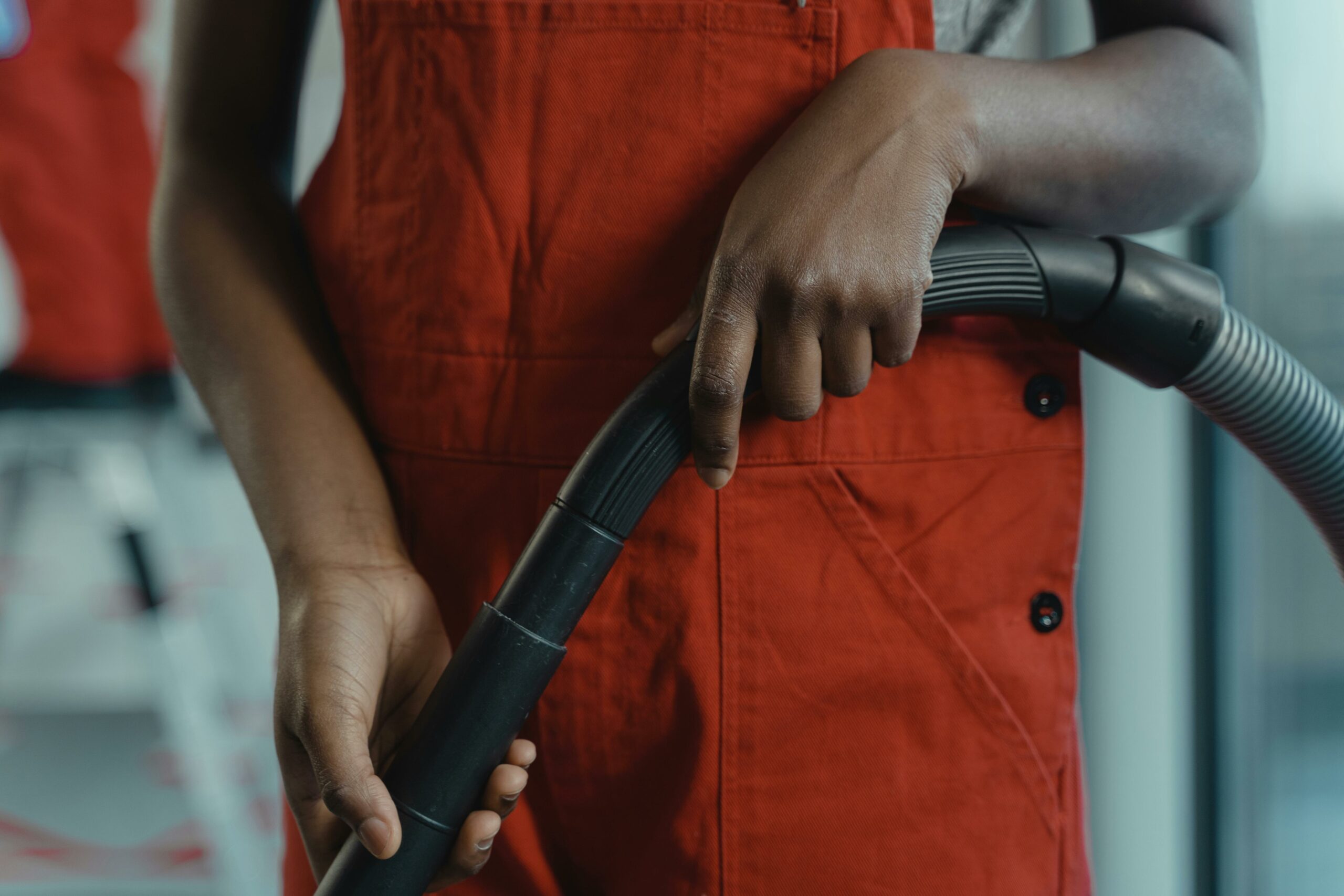 A person in a red apron holding a vacuum cleaner hose during indoor cleaning.